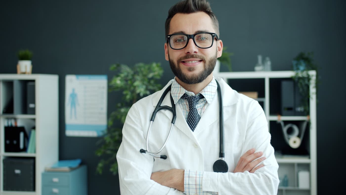 A smiling clinician in a white coat standing in a bright consulting room
