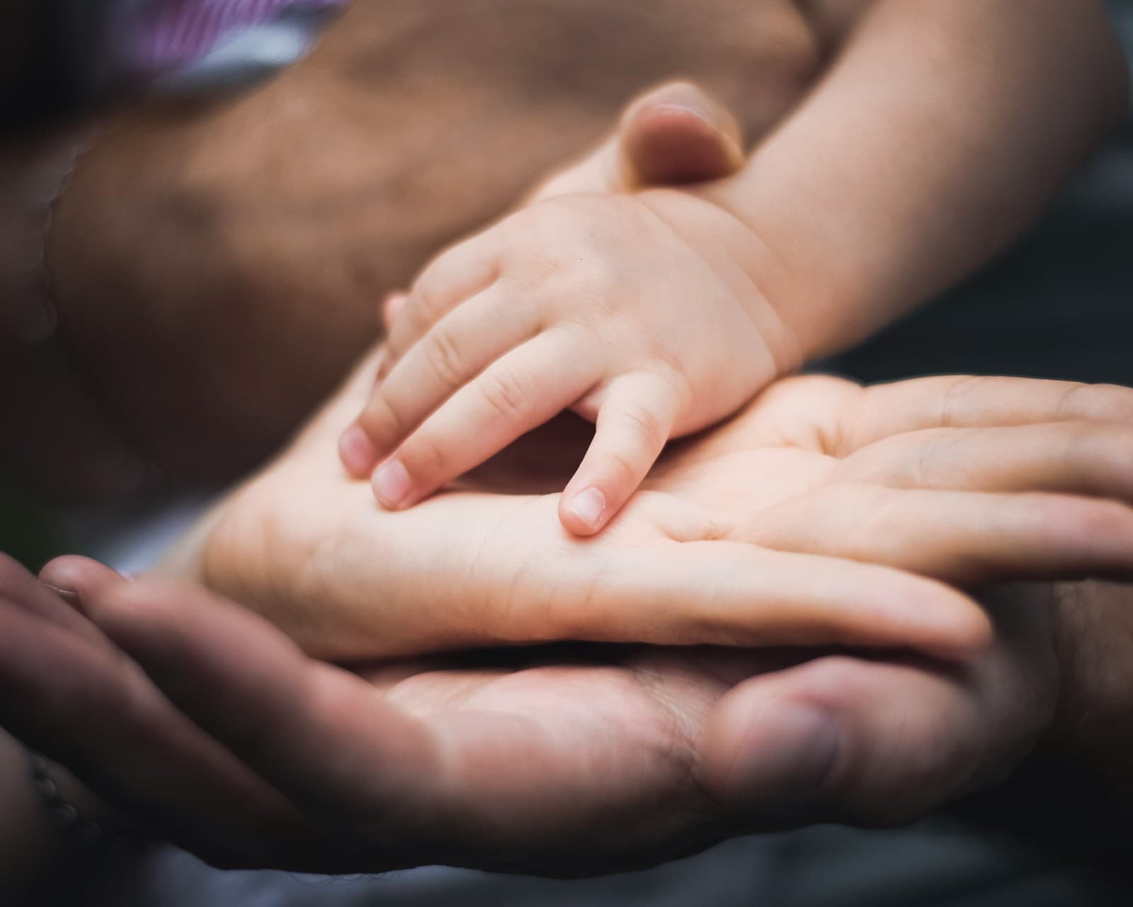 A baby's small hand resting on the open palms of two parents